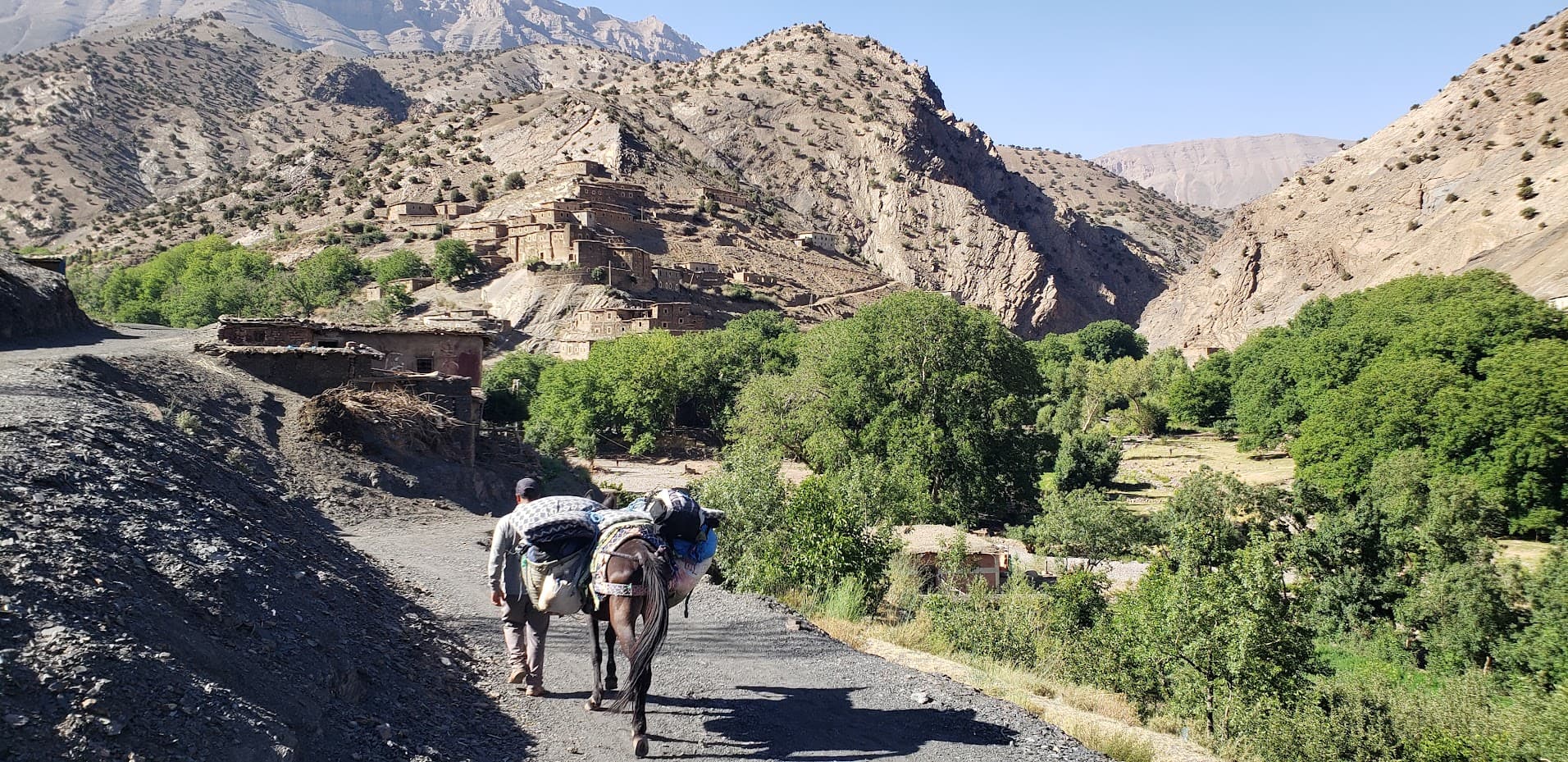 Muletier sur un sentier avec village berbère en arrière-plan